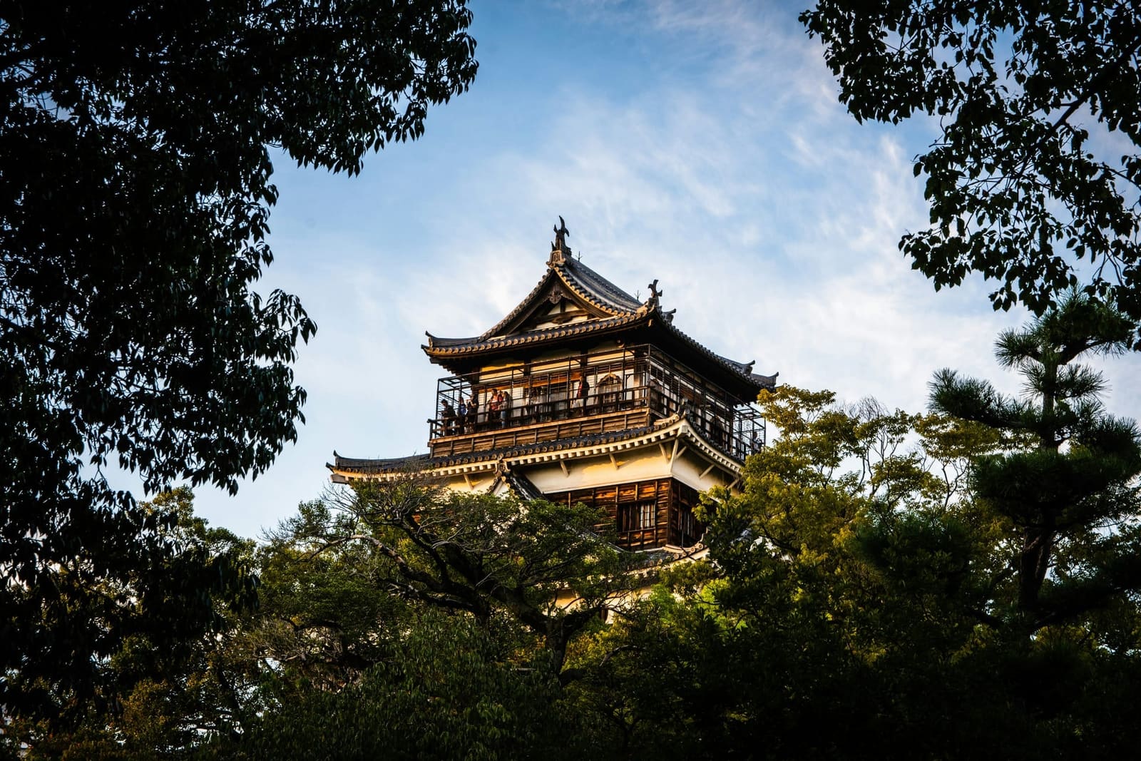Hiroshima Castle keep framed by green trees with warm evening light and blue sky, Japan
