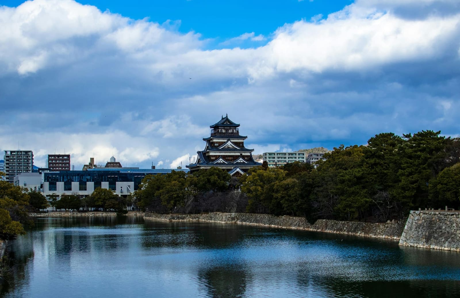 Hiroshima Castle and stone-walled moat under dramatic clouds with the surrounding city in the distance, Japan