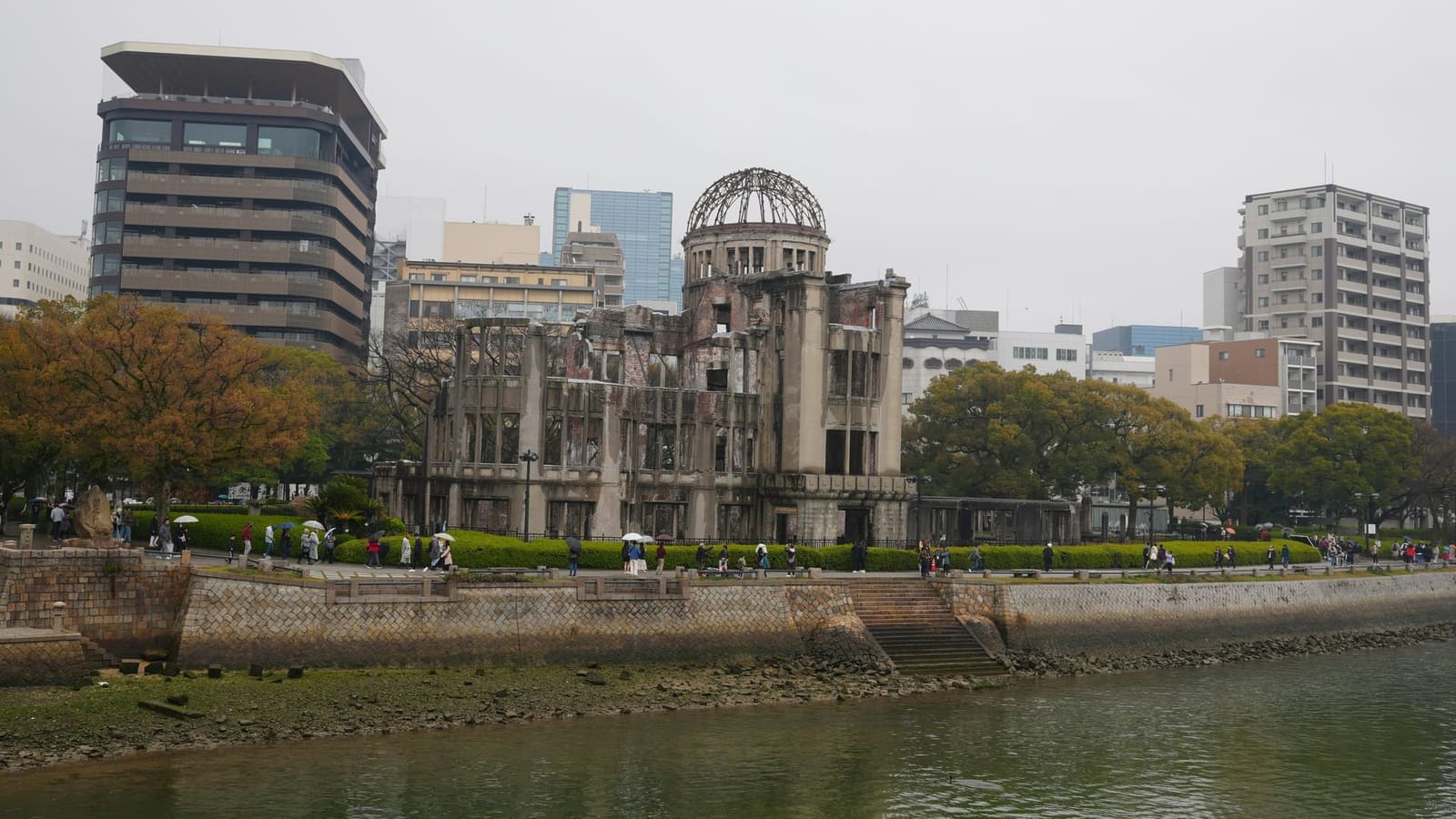 A-Bomb Dome viewed from across the Motoyasu River with visitors walking along the riverbank, Hiroshima Japan