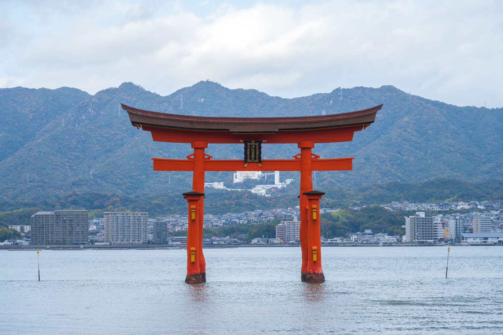 Itsukushima torii gate standing in shallow water with forested mountains in the background, Miyajima Island Japan