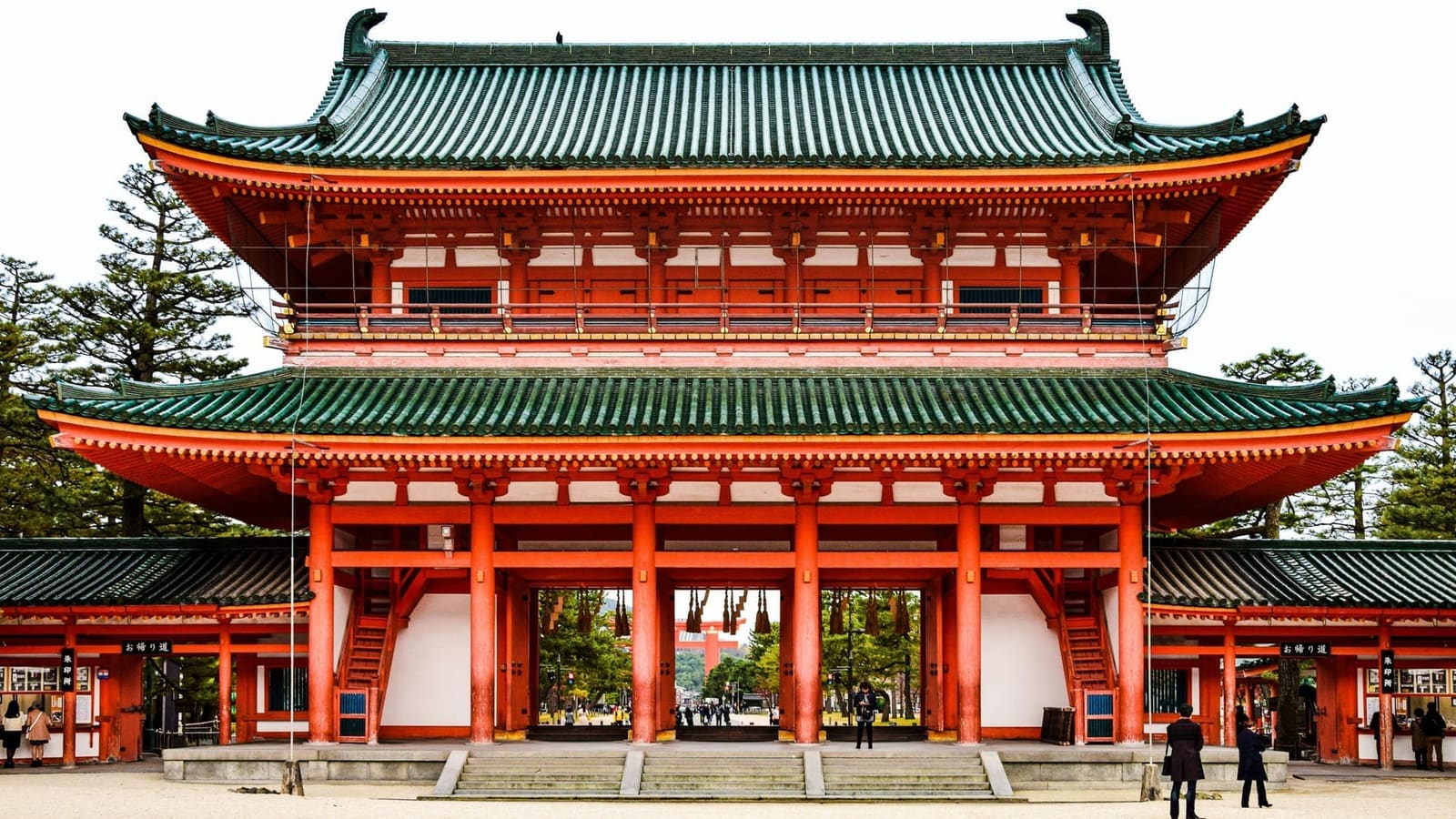 Heian Shrine's Otenmon, a two-storey vermilion gate with green tiled roofs, seen from the gravel courtyard, with the great torii visible through the central opening
