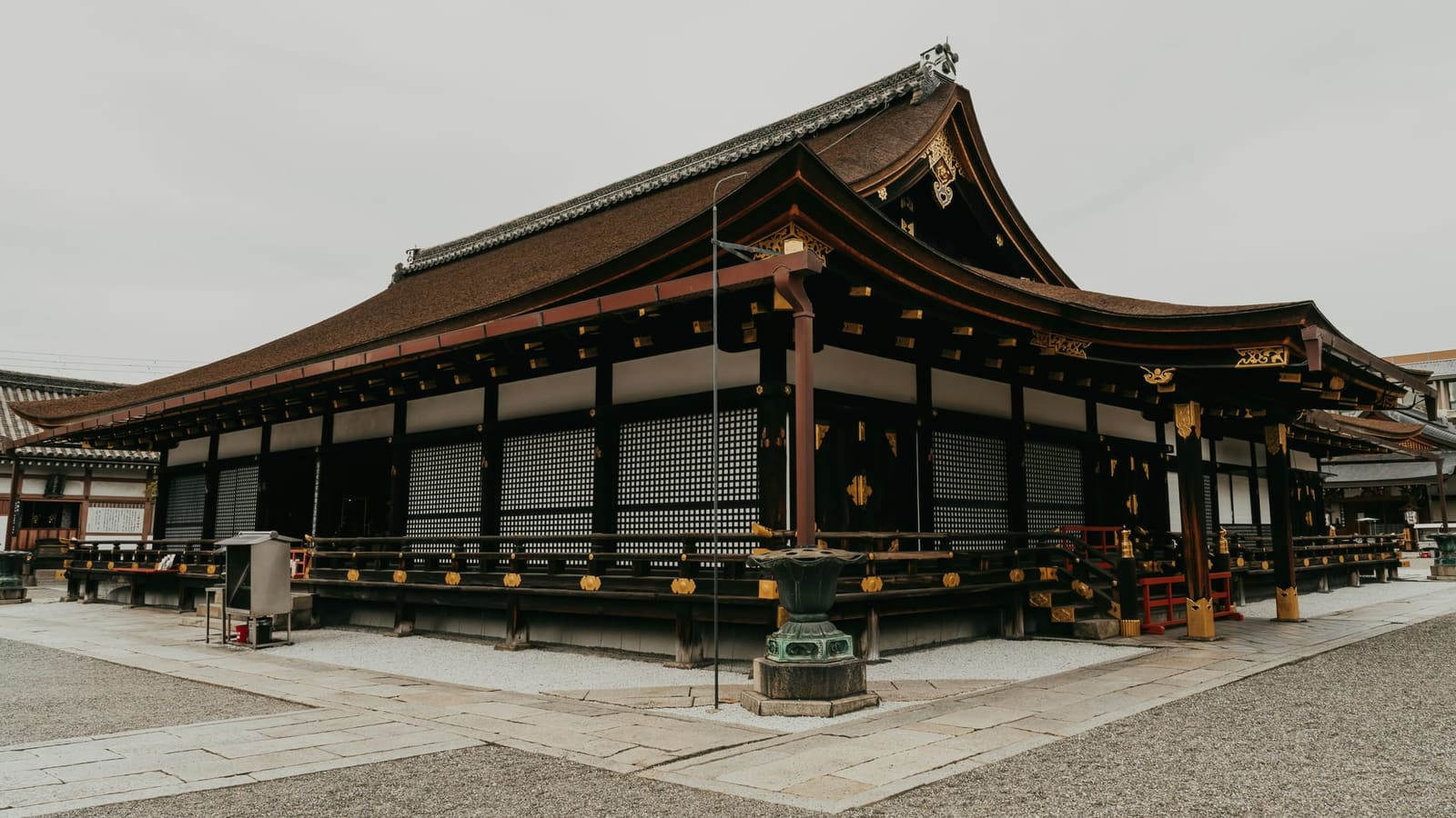 A palace hall with latticed shutters and a cypress-bark roof above a stone-paved court at the Kyoto Imperial Palace