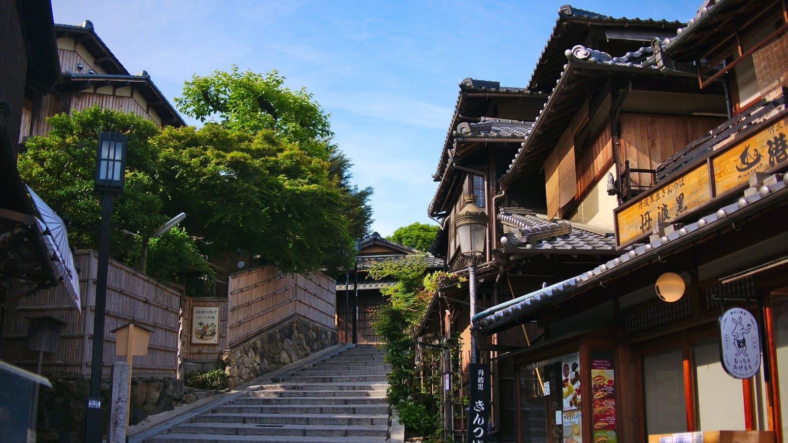 Stone steps rising between wooden shopfronts and a bamboo fence in the Sannenzaka-Ninenzaka district, on a clear morning