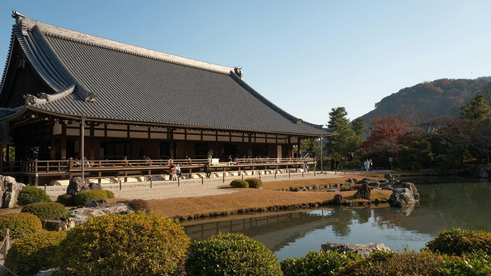 The long Hojo hall and its veranda above the Sogenchi pond in autumn, with red maples and the Arashiyama hills