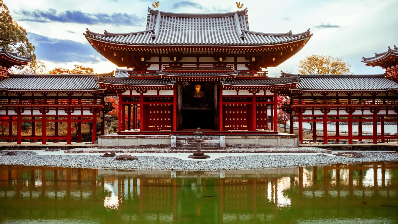 Byodo-in's Phoenix Hall seen head-on across its pond, the gilded Amida Buddha visible through the central opening, with autumn leaves behind