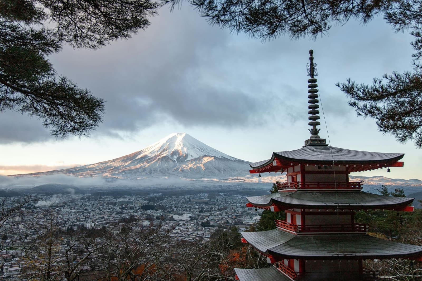 Chureito Pagoda in the foreground with snow-capped Mount Fuji above Fujiyoshida under a cloudy sky