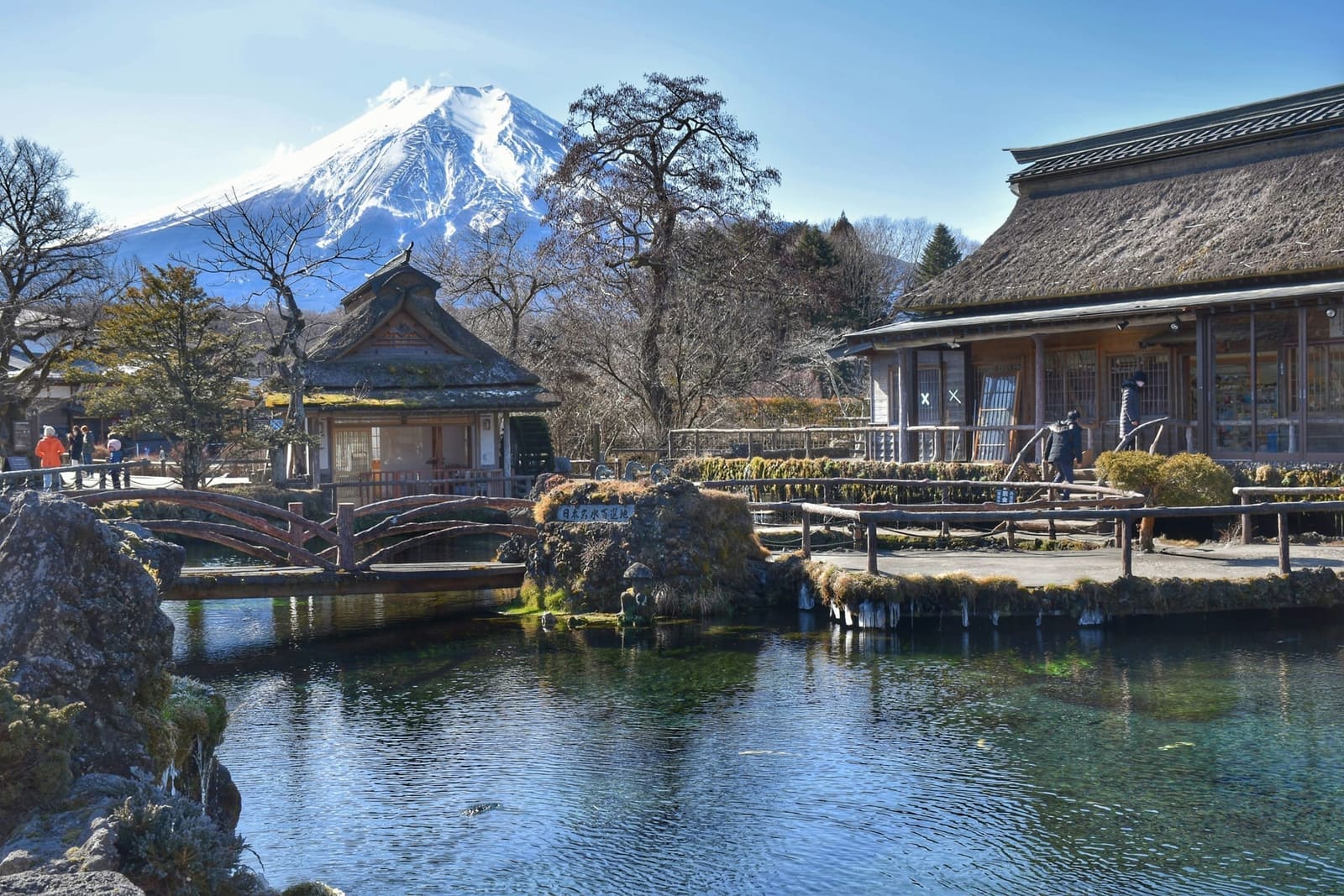 Thatched-roof buildings beside a clear spring pond at Oshino Hakkai with snow-capped Mount Fuji behind