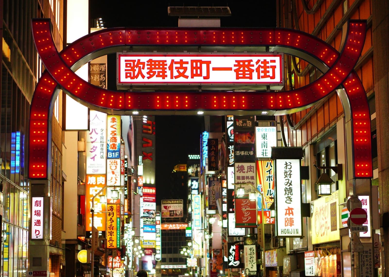 Kabukicho entertainment district entrance arch glowing with red neon lights and Japanese signs at night in Shinjuku