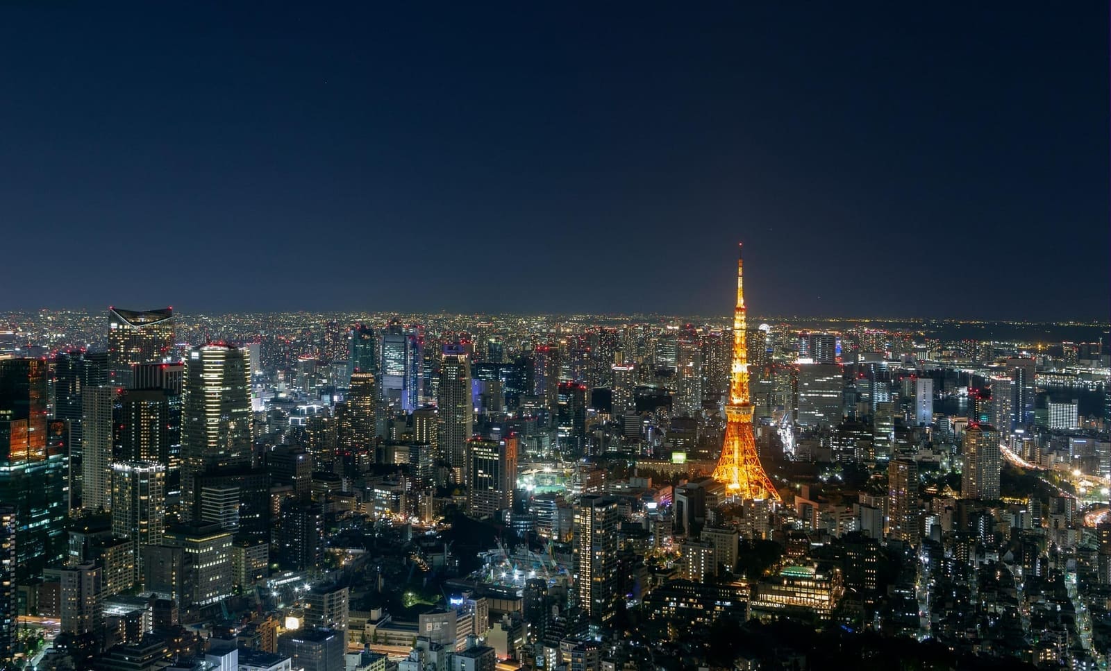 Tokyo Tower glowing orange at night surrounded by the illuminated city skyline from above