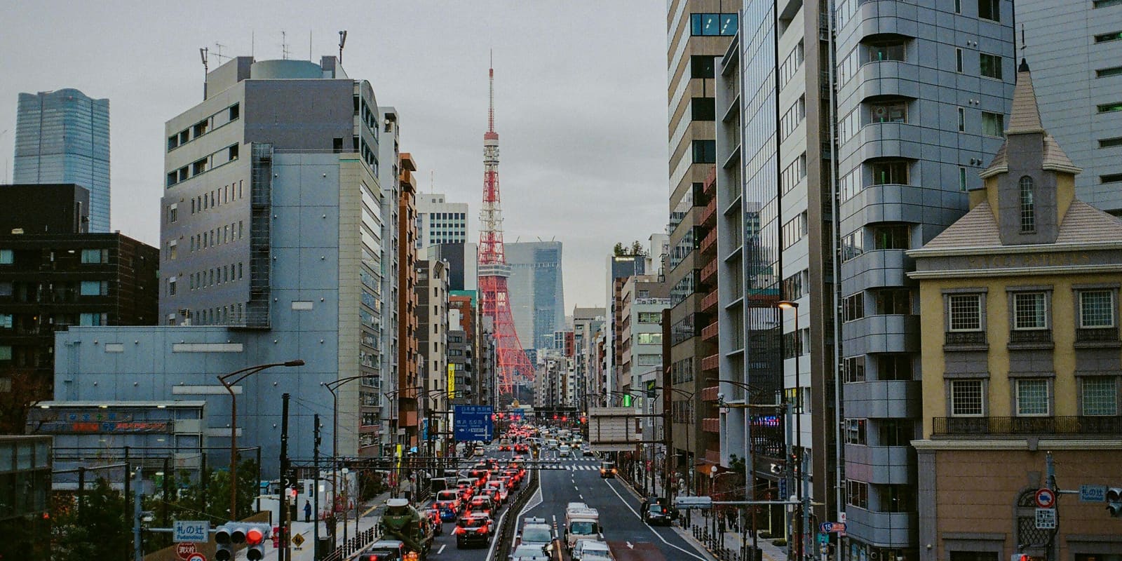 Tokyo Tower rising at the end of a busy city avenue lined with office buildings and hotels