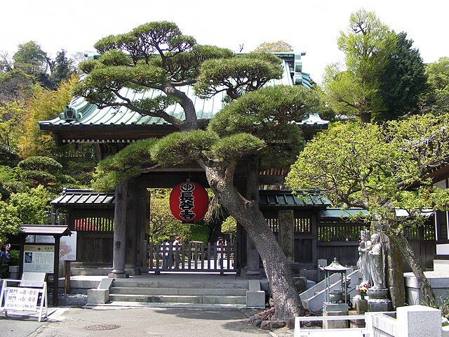 Sanmon gate at Hasedera Temple in Kamakura, framed by a pine tree with a paper lantern and stone statues nearby