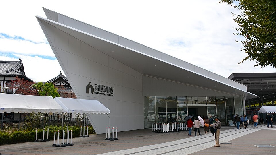 The angular white entrance building of the Kyoto Railway Museum, with its name on the wall and a traditional wooden building to the left