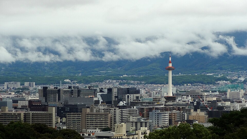 Kyoto Tower seen from a distance, standing above the low city with cloud on the mountains behind
