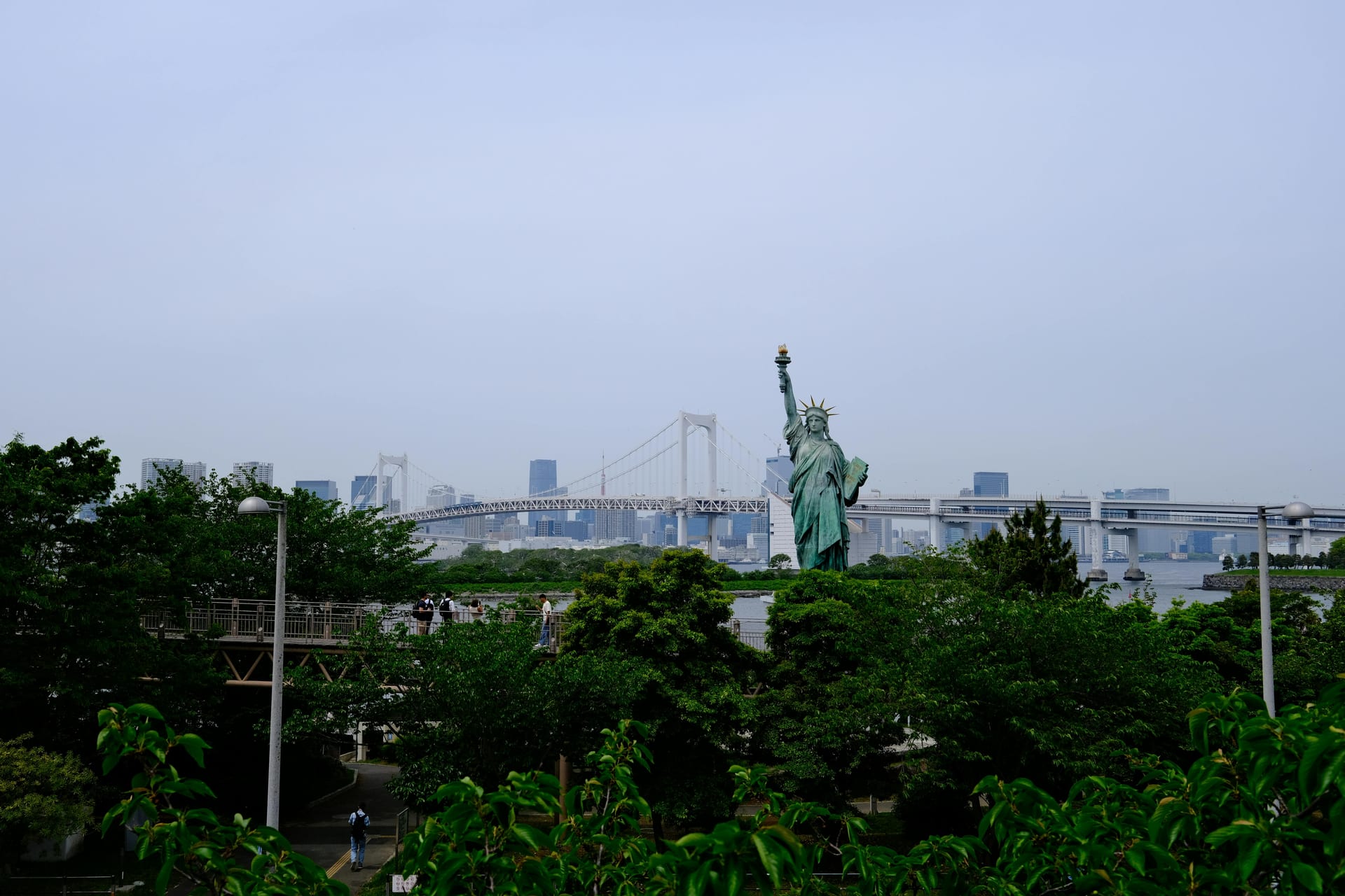 The Statue of Liberty replica on Odaiba's waterfront with Rainbow Bridge and the Tokyo skyline behind it
